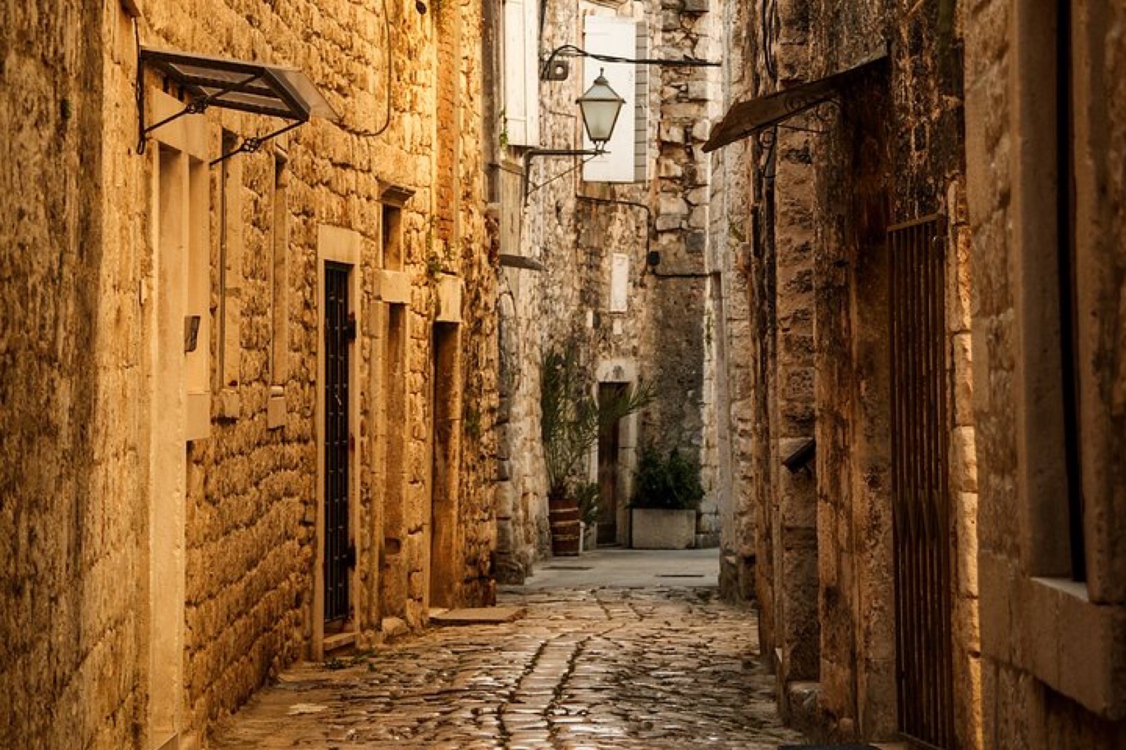 Narrow honey-coloured stone alley in medieval Trogir bathed in afternoon light